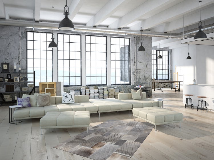 Velký otevřený loft v industriálním stylu s vysokými stropy, velkými okny s příčkami, betonovými stěnami, dřevěnou podlahou a moderní pohovkou.
