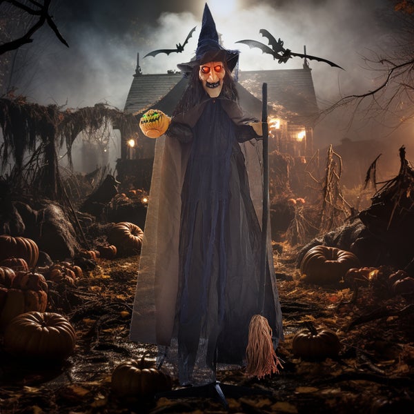 Dekorativní halloweenská scéna s figurkou čarodějnice, dýněmi a strašidelným domem v pozadí.