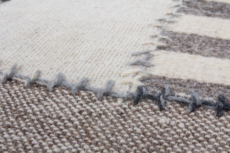 Detail tkaného koberce s viditelnými švy a texturovaným povrchem.