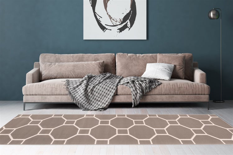 Obývací pokoj s moderní pohovkou, károvanou dekou a obdélníkovým kobercem s geometrickým šestiúhelníkovým vzorem na dřevěné podlaze.