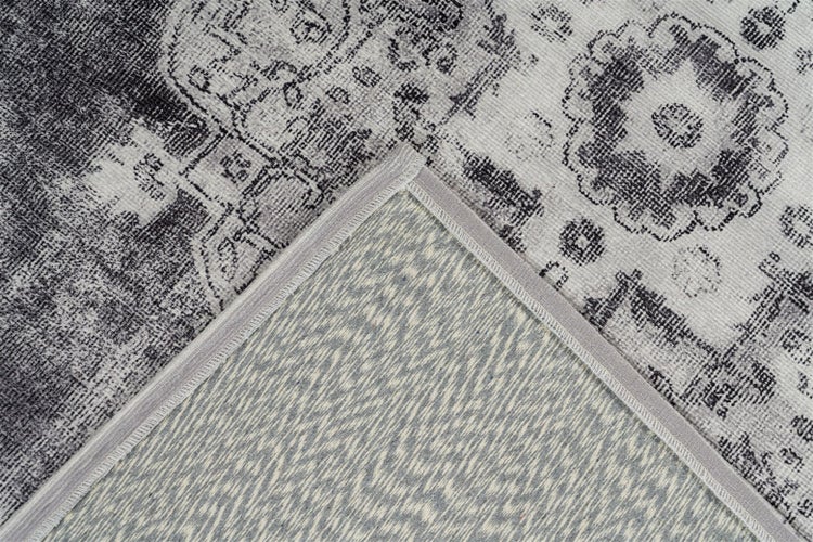 Detailní záběr vintage koberce s orientálním vzorem, viditelnou zadní stranou a obšitým okrajem.