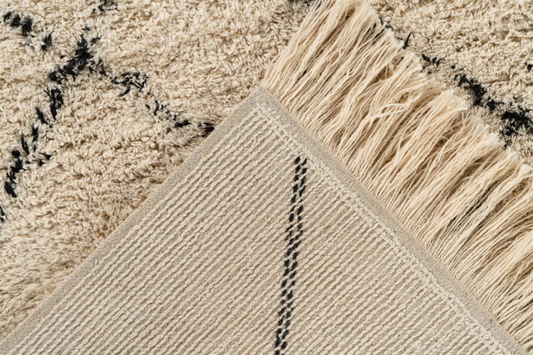 Detail koberce s vysokým vlasem s třásněmi, geometrickým vzorem a tkanou zadní stranou.