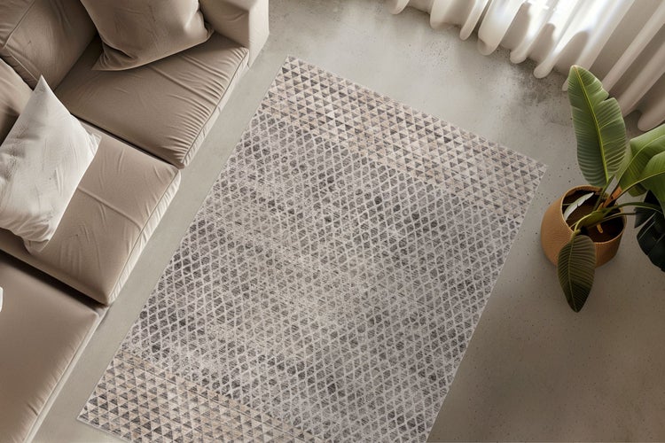 Obývací pokoj s obdélníkovým kobercem s geometrickým vzorem trojúhelníků před pohovkou vedle pokojové rostliny na betonové podlaze.