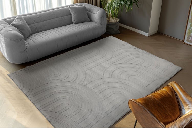 Obývací pokoj v moderním stylu, šedý koberec s geometrickým vzorem oblouků, pohovka a kožené křeslo na parketové podlaze.