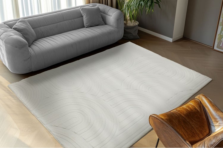 Moderní obývací koberec s geometrickým reliéfním vzorem na podlaze z rybí kosti před pohovkou.