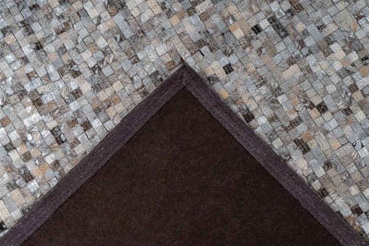Detailní pohled na patchworkový koberec ze čtvercových kožených kousků s metalickým efektem a viditelnými švy.