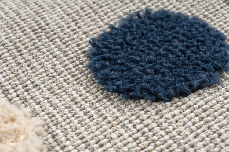 Detailní záběr struktury koberce s tkaným vzorem a kulatými prvky z materiálu s vysokým vlasem.