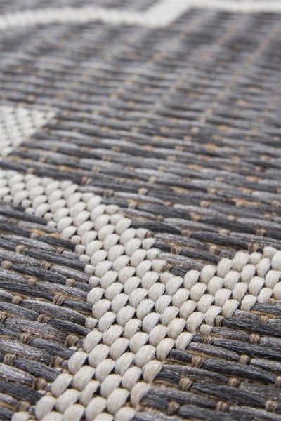 Detail strukturovaného povrchu tkaného koberce s geometrickým vzorem.