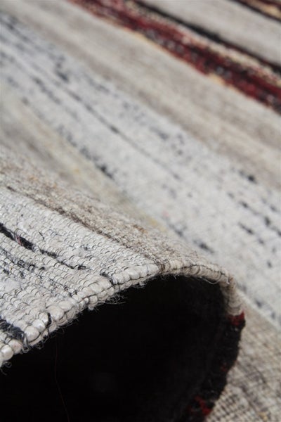 Detailní záběr na plochý tkaný koberec s proužkovaným vzorem a viditelnou zadní stranou na okraji.