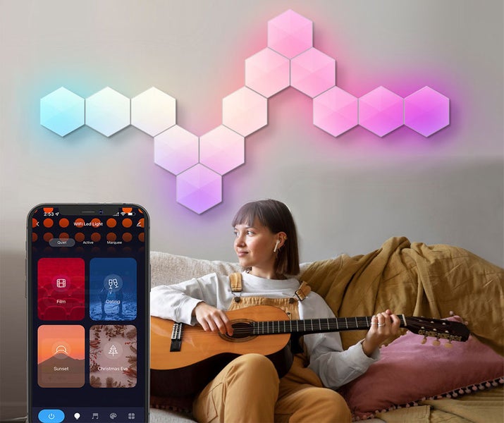 Wi-Fi LED nástěnné panely v šestiúhelníkovém tvaru, ovládané přes aplikaci v telefonu, jako dekorativní osvětlení za osobou s kytarou na pohovce.