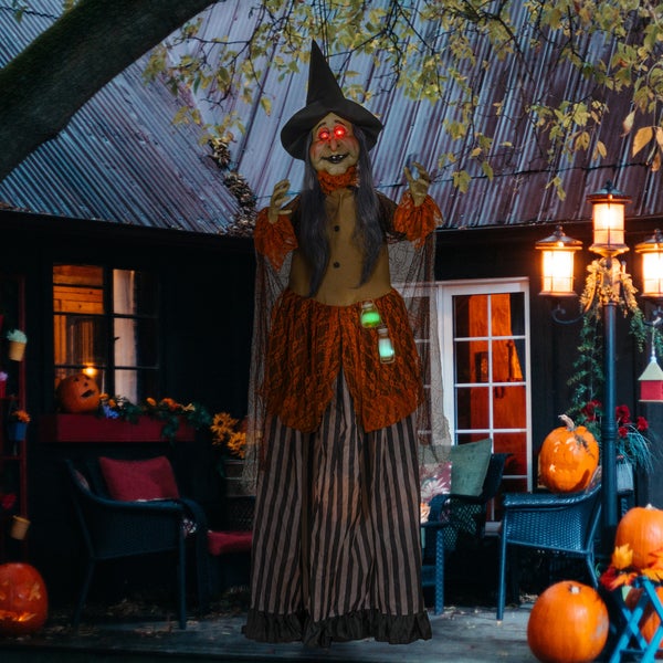 Dekorativní halloweenská scéna s animovanou figurkou čarodějnice a dýněmi před domem.