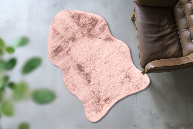 Umělá kožešina v organickém tvaru na betonové podlaze vedle koženého křesla.