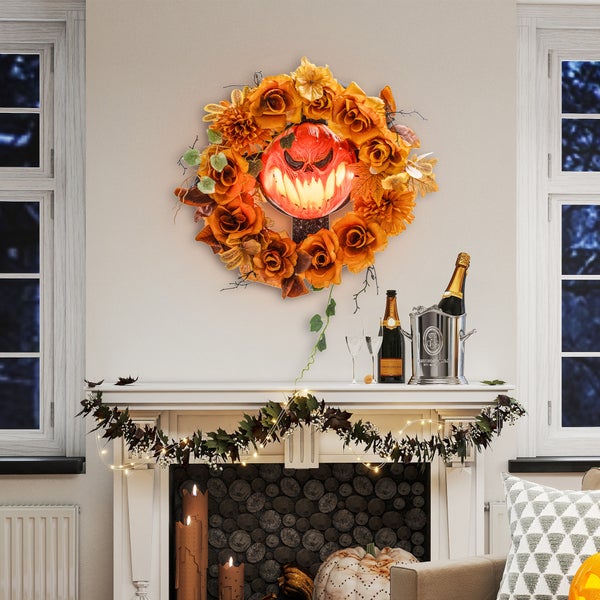 Halloweenská dekorace s květinovým věncem, dýňovou lucernou, girlandou a šampaňským na římse krbu.