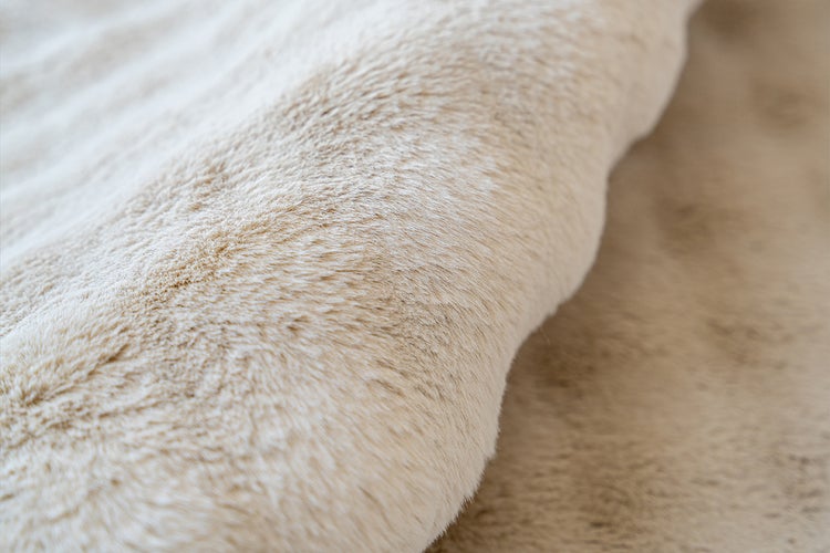 Detailní záběr na měkký, béžový materiál z umělé kožešiny s huňatou texturou.