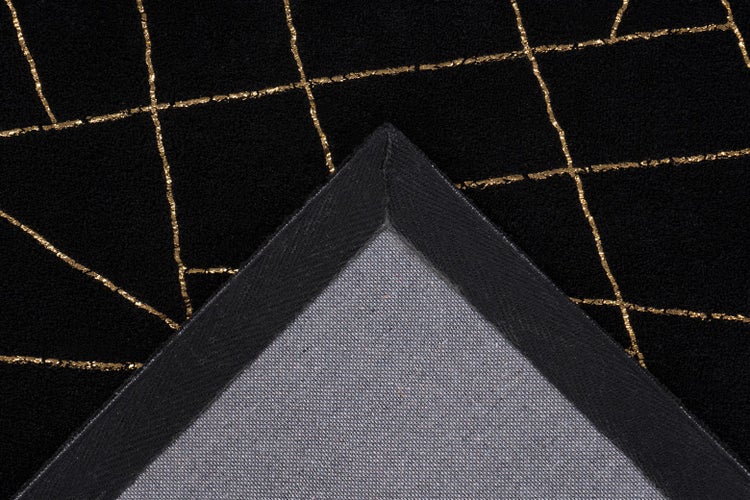 Detailní pohled na koberec se zlatým geometrickým vzorem linií na černém podkladu a strukturovanou zadní stranou na přehnutém rohu.