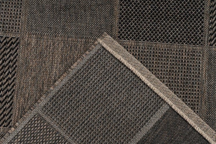 Detail plochého tkaného koberce s patchworkovým vzorem geometrických motivů a zahnutým rohem s obšitým okrajem.
